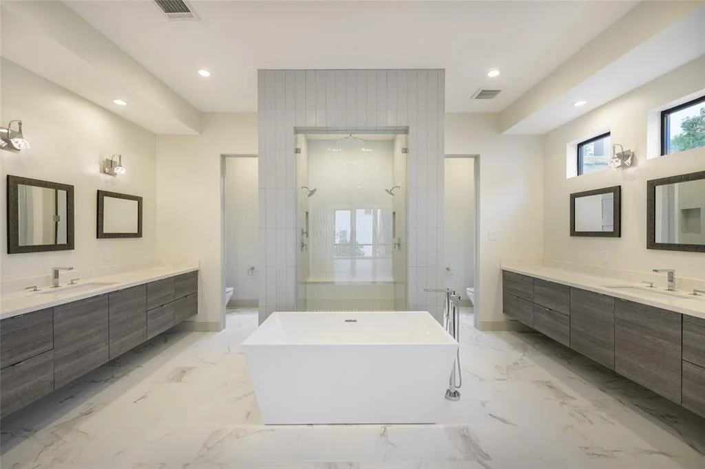 Modern bathroom with dual sinks, large mirror frames, a central bathtub, and a glass-enclosed shower in the background.