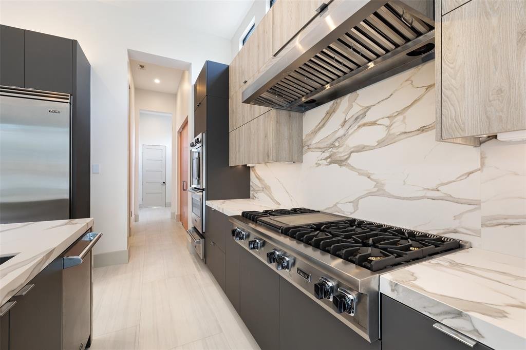 Modern kitchen with marble backsplash, gray cabinetry, and professional stainless steel stove with four burners.