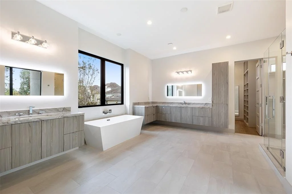 Modern bathroom with light wood cabinetry, a free-standing bathtub, large windows, and a glass shower enclosure.