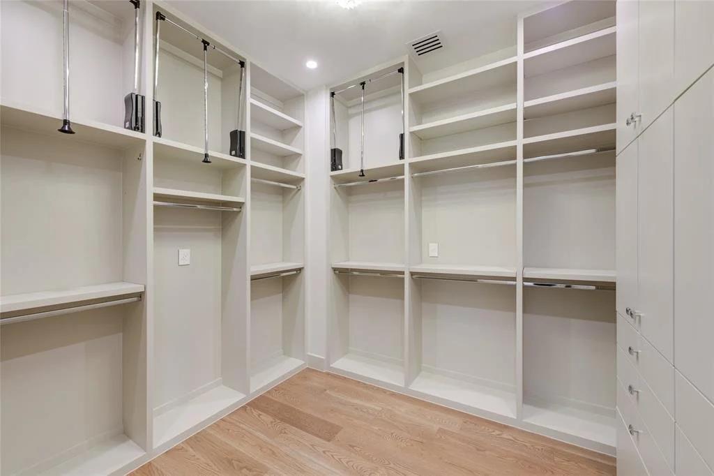 Empty walk-in closet with white built-in shelves, hanging rods, and drawers, and a wooden floor.