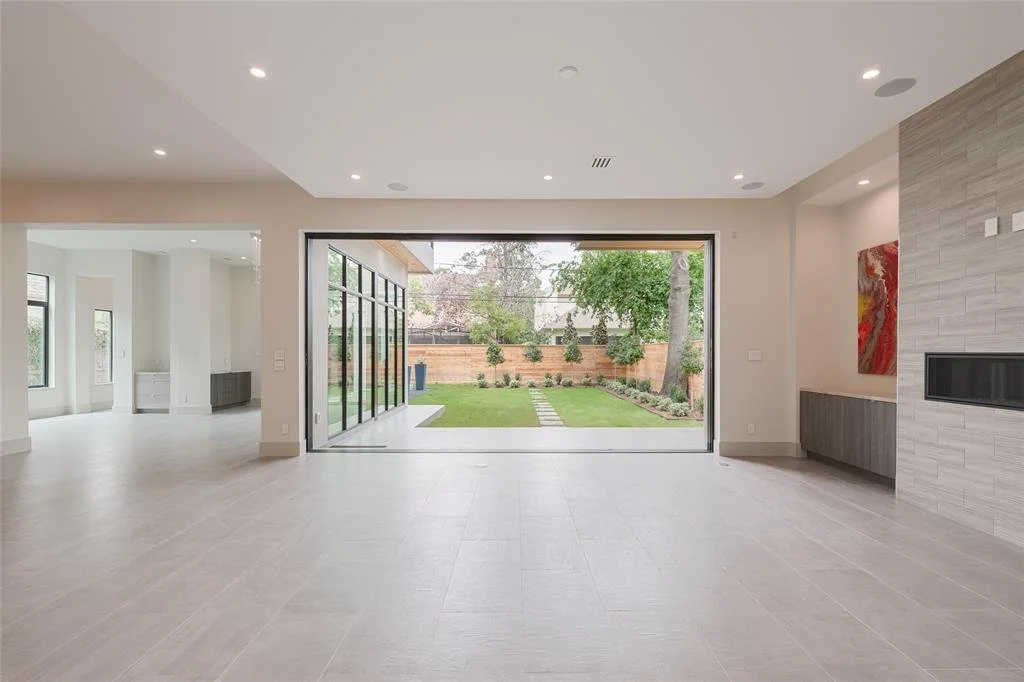 Empty modern living room with large sliding glass doors opening to a backyard with grass, trees, and a stone pathway.