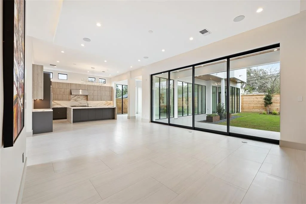 An empty modern living room with large glass sliding doors opening to a backyard with grass and a wooden fence.
