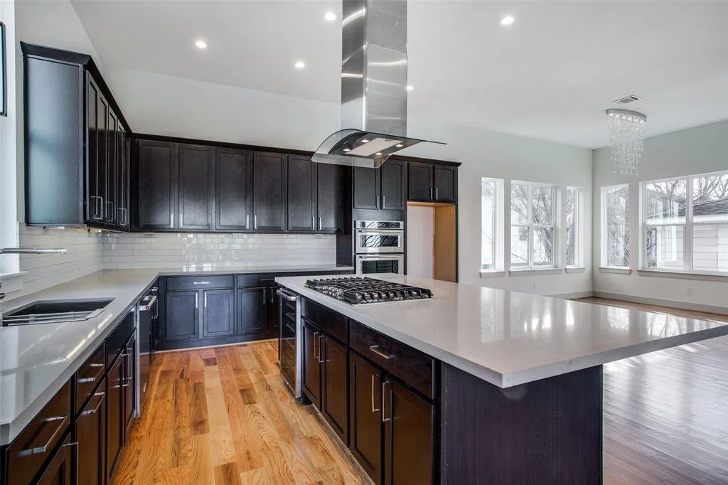 A modern kitchen with dark wooden cabinets, a white countertop, a gas stove on an island, and stainless steel appliances.