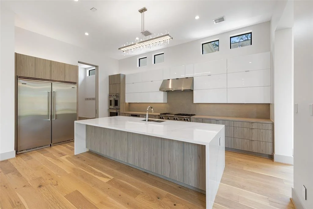 Modern kitchen with white and light wood cabinetry, stainless steel refrigerator, stove, and range hood, and an island with a white countertop.
