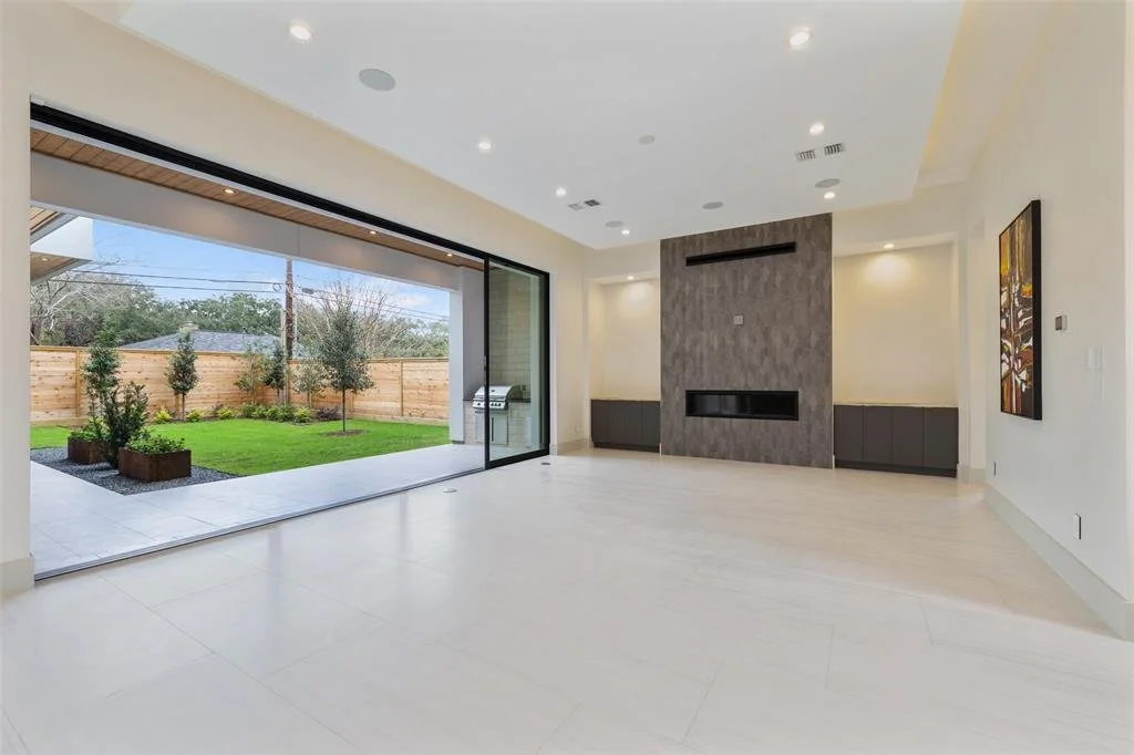 Empty living room with large sliding glass door opening to a backyard with a lawn, trees, and a wooden fence.