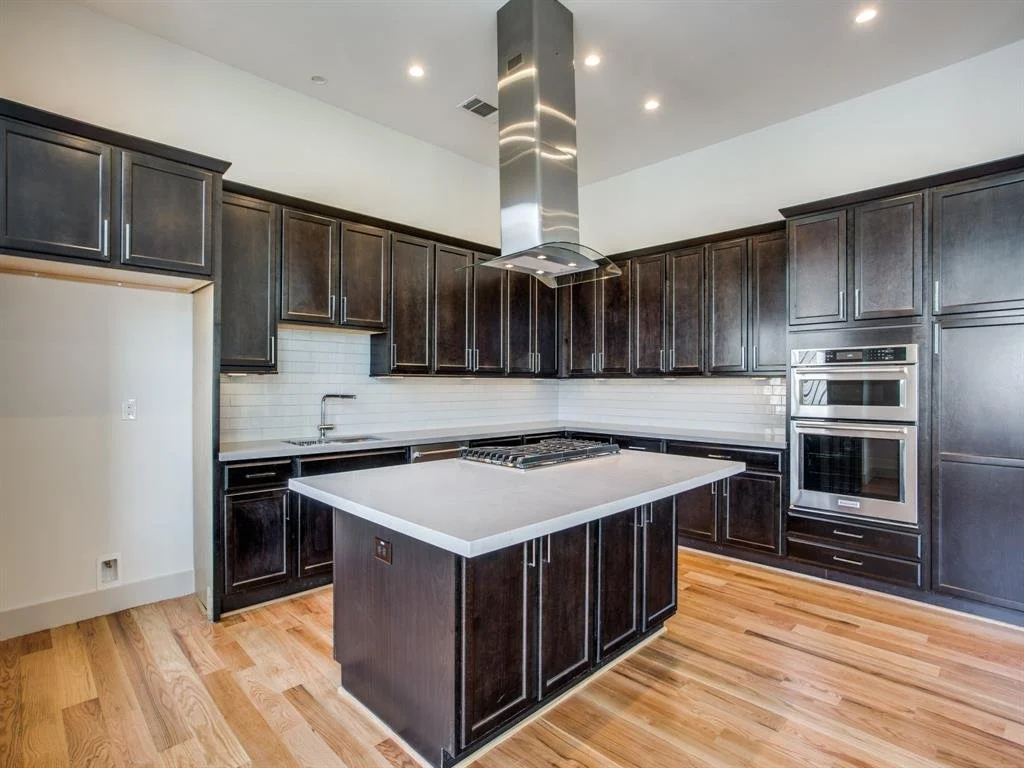 Modern kitchen with dark wood cabinets, white subway tile backsplash, stainless steel appliances, a kitchen island with a white countertop, and hardwood flooring.