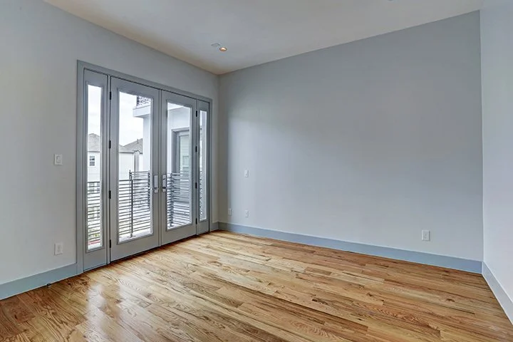 Empty room with wooden floors, white walls, and glass doors leading to a balcony.