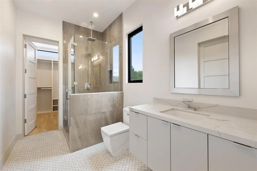 Modern bathroom with shower enclosed in glass, white vanity with marble countertop, and a toilet.