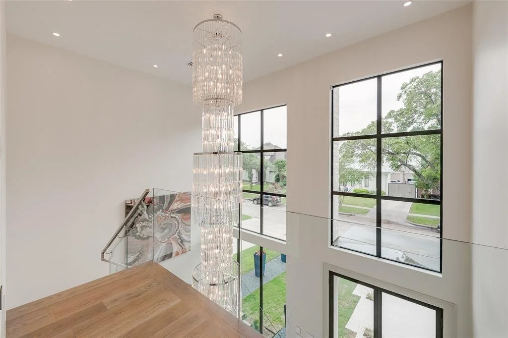 Interior view of a modern house's upper level with large windows, a chandelier, and a wooden floor.