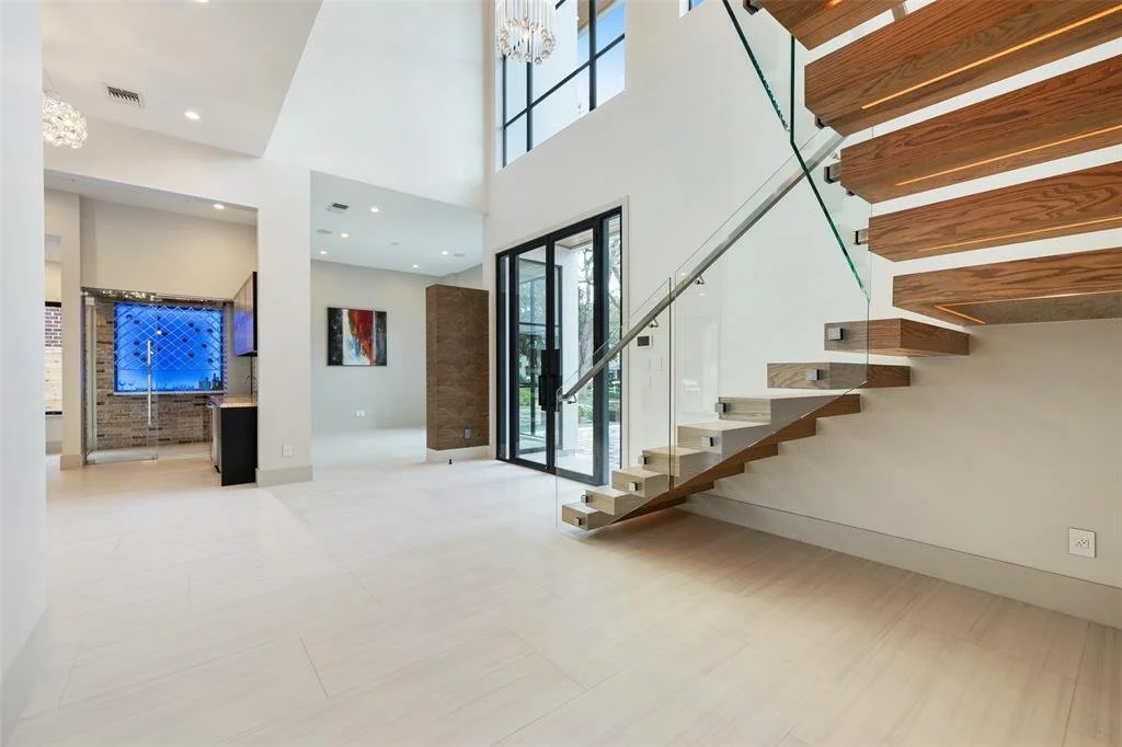 Modern interior living space with a floating staircase with wooden steps, glass railing, large glass doors, and minimalist decor.