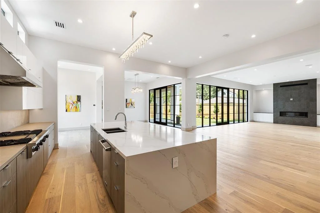 Open-concept kitchen and living room with large windows, hardwood floors, and modern furnishings.