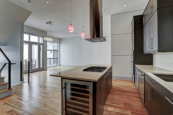 Modern open-concept kitchen with dark cabinetry, stainless steel appliances, a kitchen island with a gas cooktop, and large windows and doors leading to a balcony.