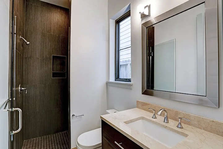 Modern bathroom with a walk-in shower, a window, a toilet, and a vanity with a mirror.