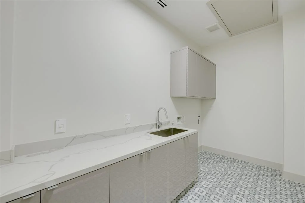 Empty modern laundry room with white walls, marble countertop, cabinets, and a stainless steel sink.