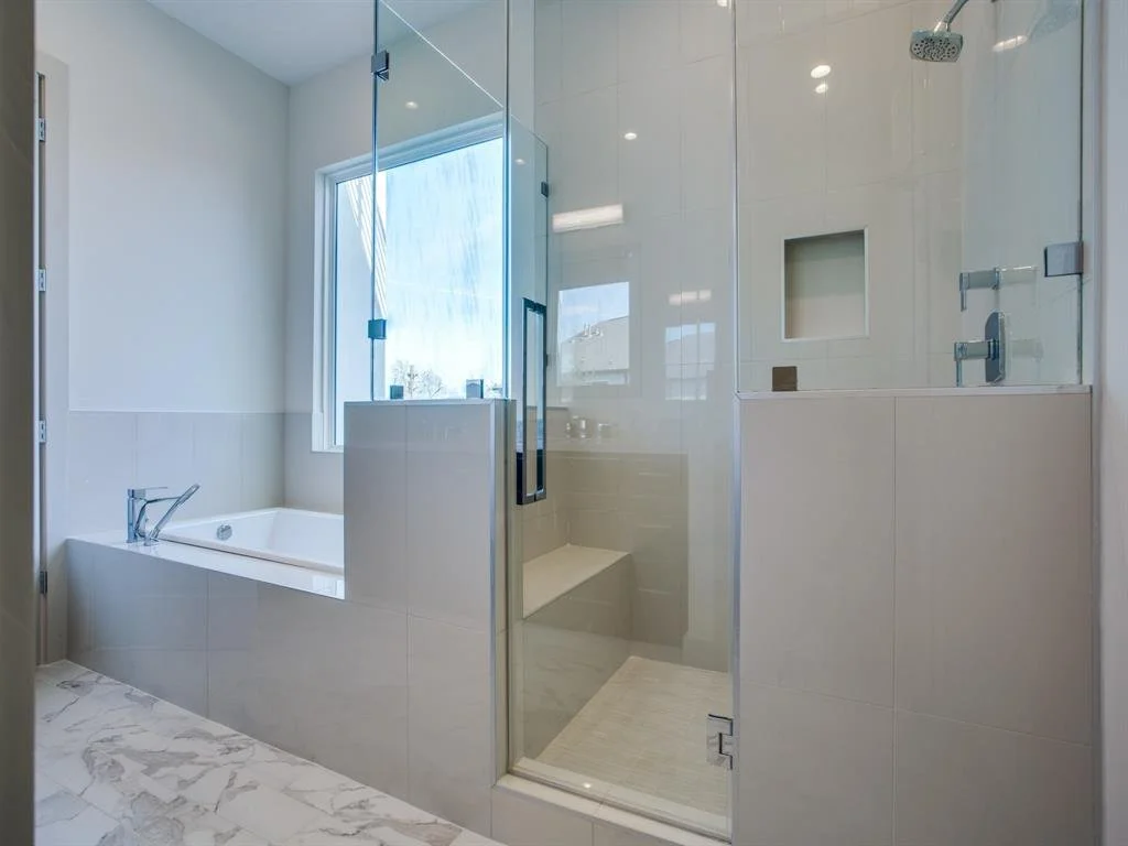Modern bathroom featuring a bathtub beneath a window, a glass shower enclosure with a bench, and white tiled walls.