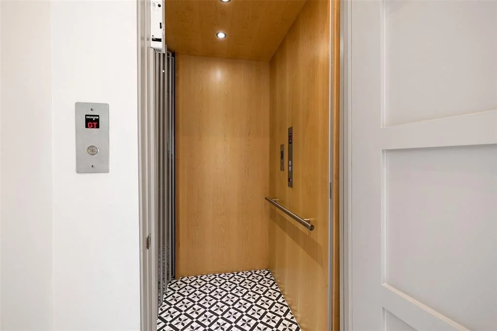 Empty elevator with wooden walls, patterned tile floor, and control panels on the right side.