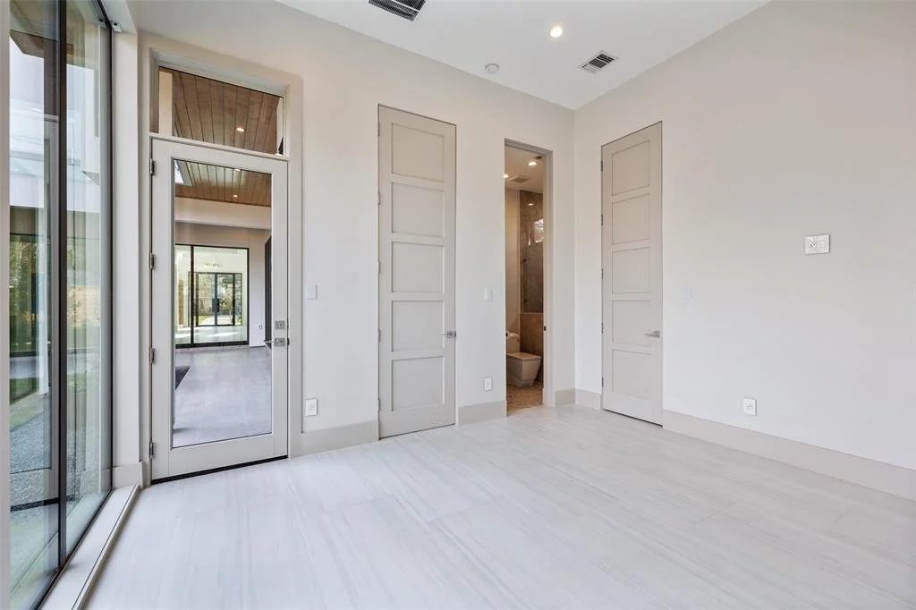 Empty room with large glass door, two closed closet doors, and an open door leading to a bathroom.