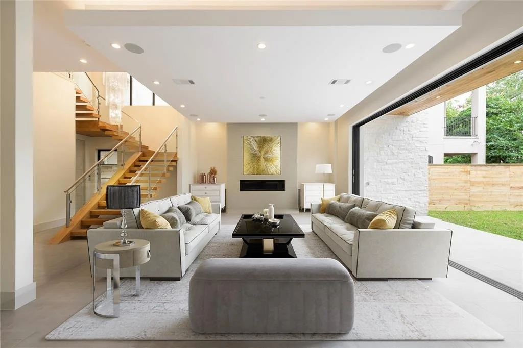 Modern living room with white sofas, black coffee table, gray armchair, side tables, and large sliding glass doors leading outside.