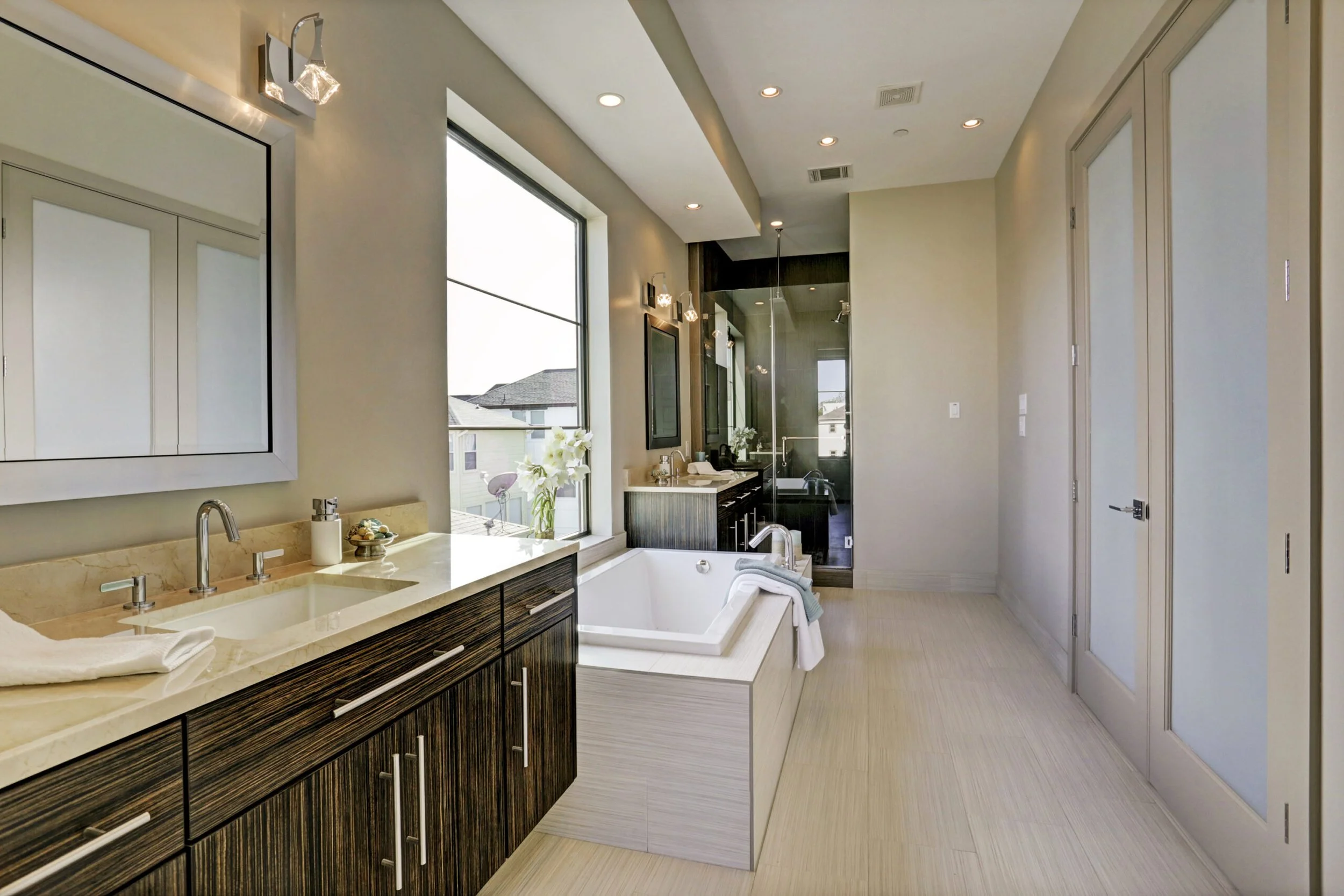 Modern bathroom with dual sinks, a large bathtub, and a shower with glass enclosure, natural light, and minimalist decor.