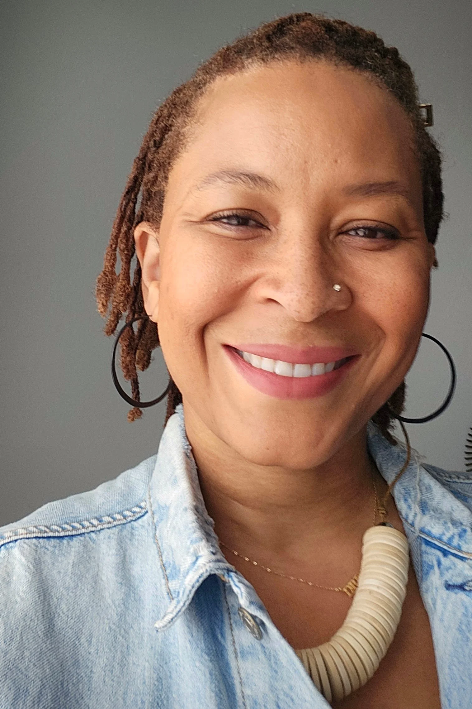 Photo of Marlo David. She is a light brown skinned Black woman with a nose ring and short locs.