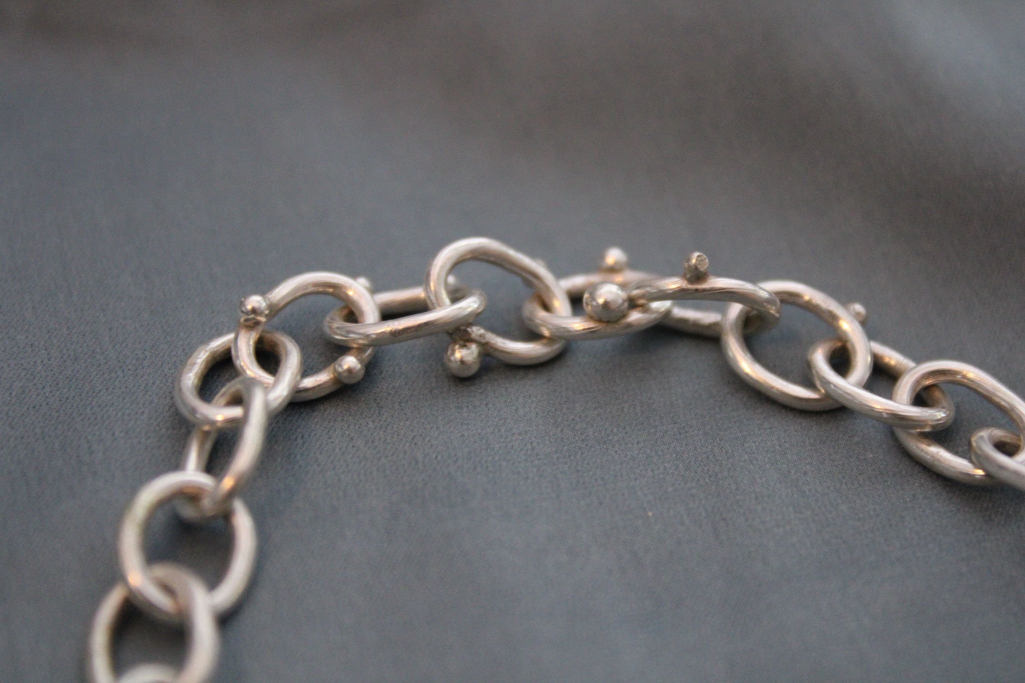 The Blobby Chain bracelet lies open on a blue satin. The Blobby Chain bracelet consists of chunky links adorned with organic granulation blobs.