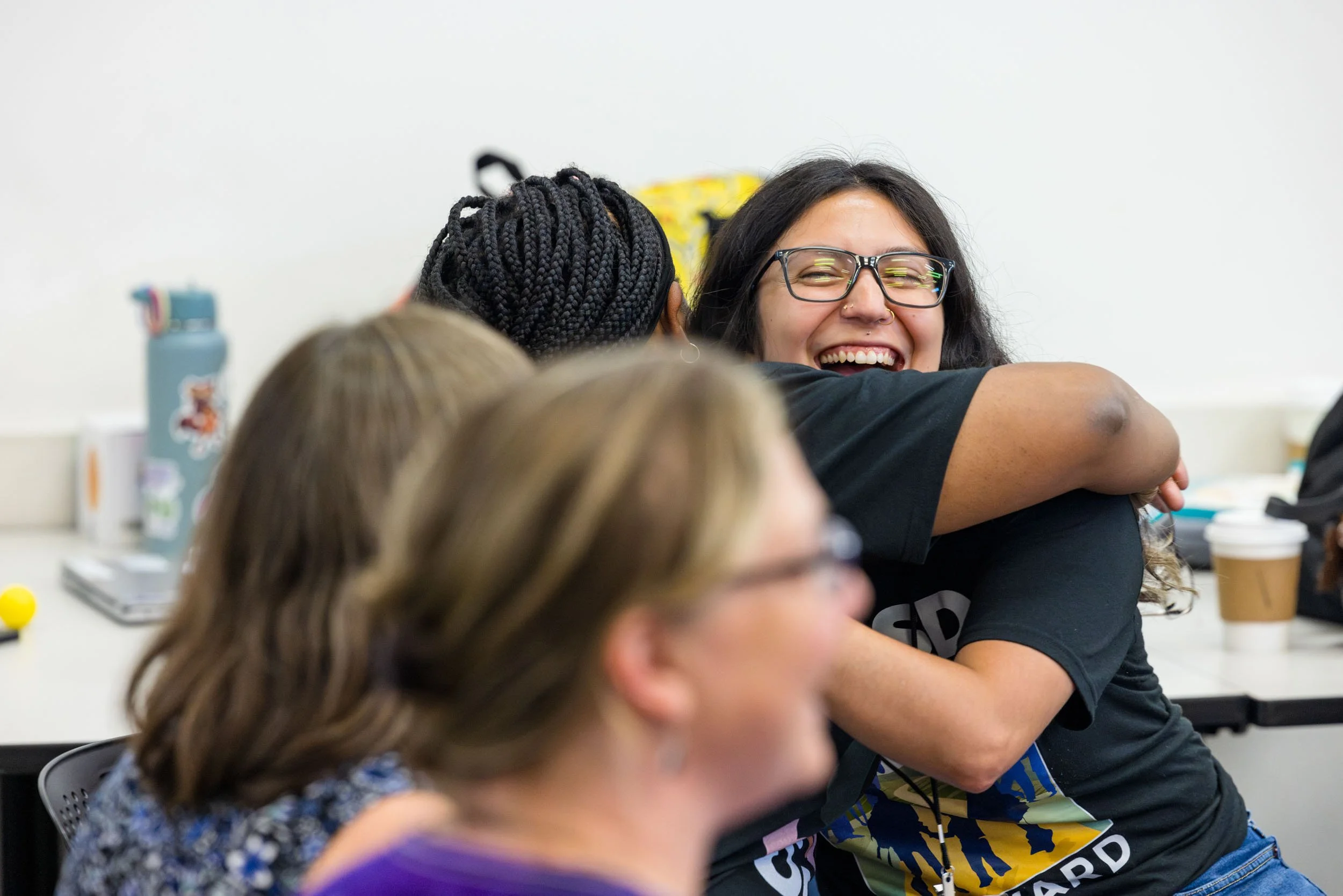 Group of women hugging and smiling during a social gathering in an indoor setting.