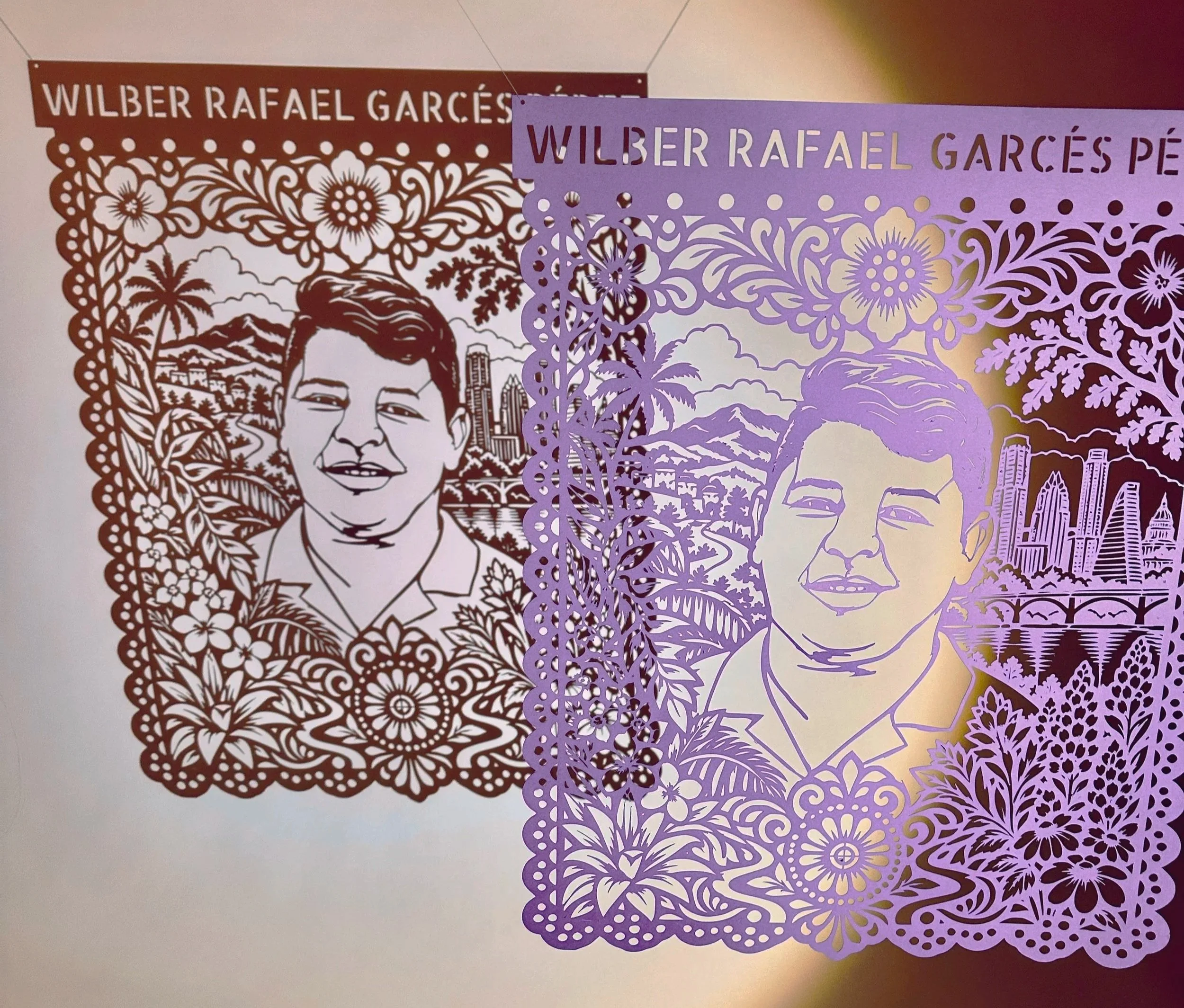 Wilber Rafael Garces Perez's portrail in papel picado hanging with the shadow of the cutout on the wall behind it.