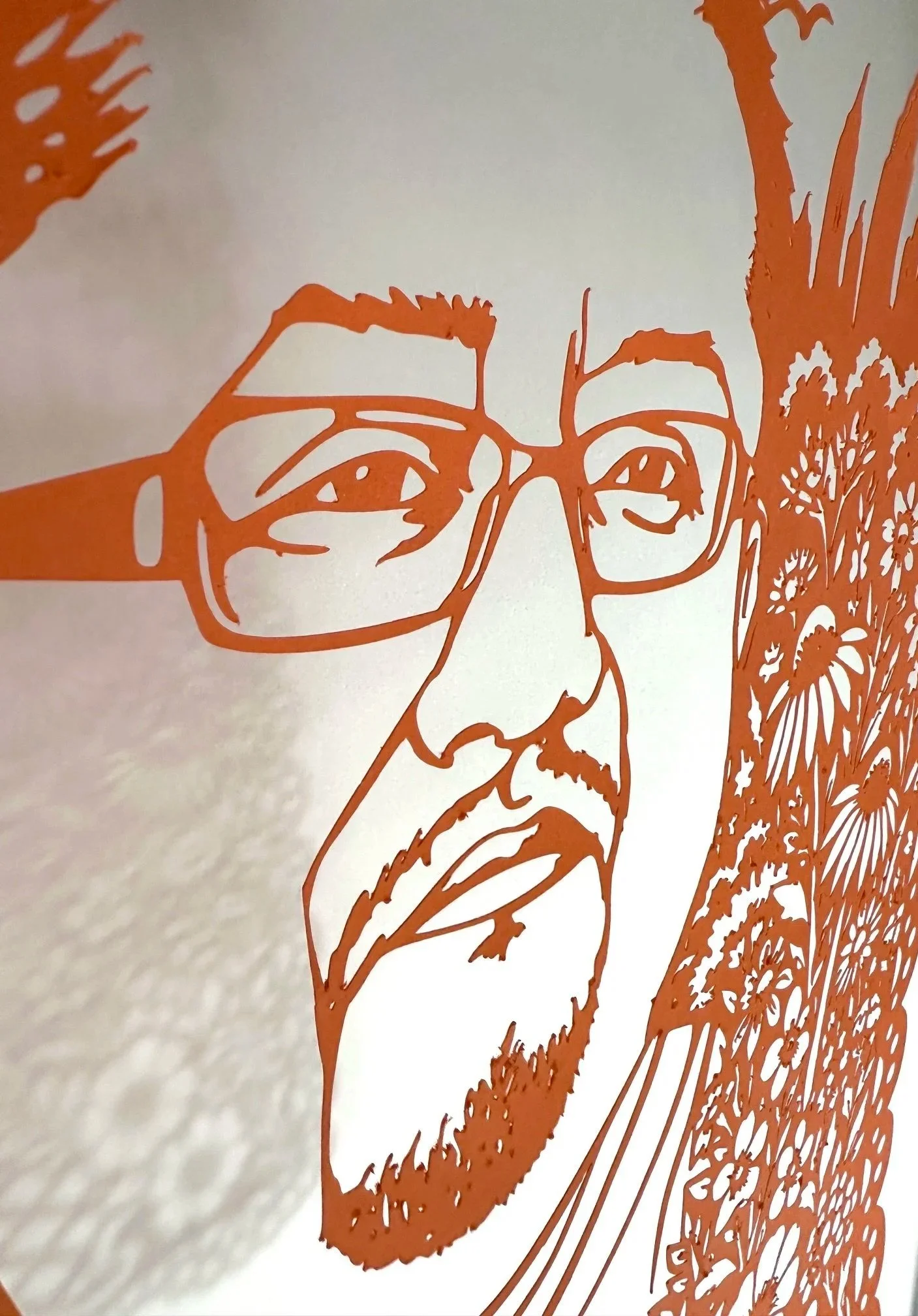 Angled close up of Edwin Jeovanny López Cornejo’s orange papel picado portrait, showing his face, glasses, and detailed floral cutwork.