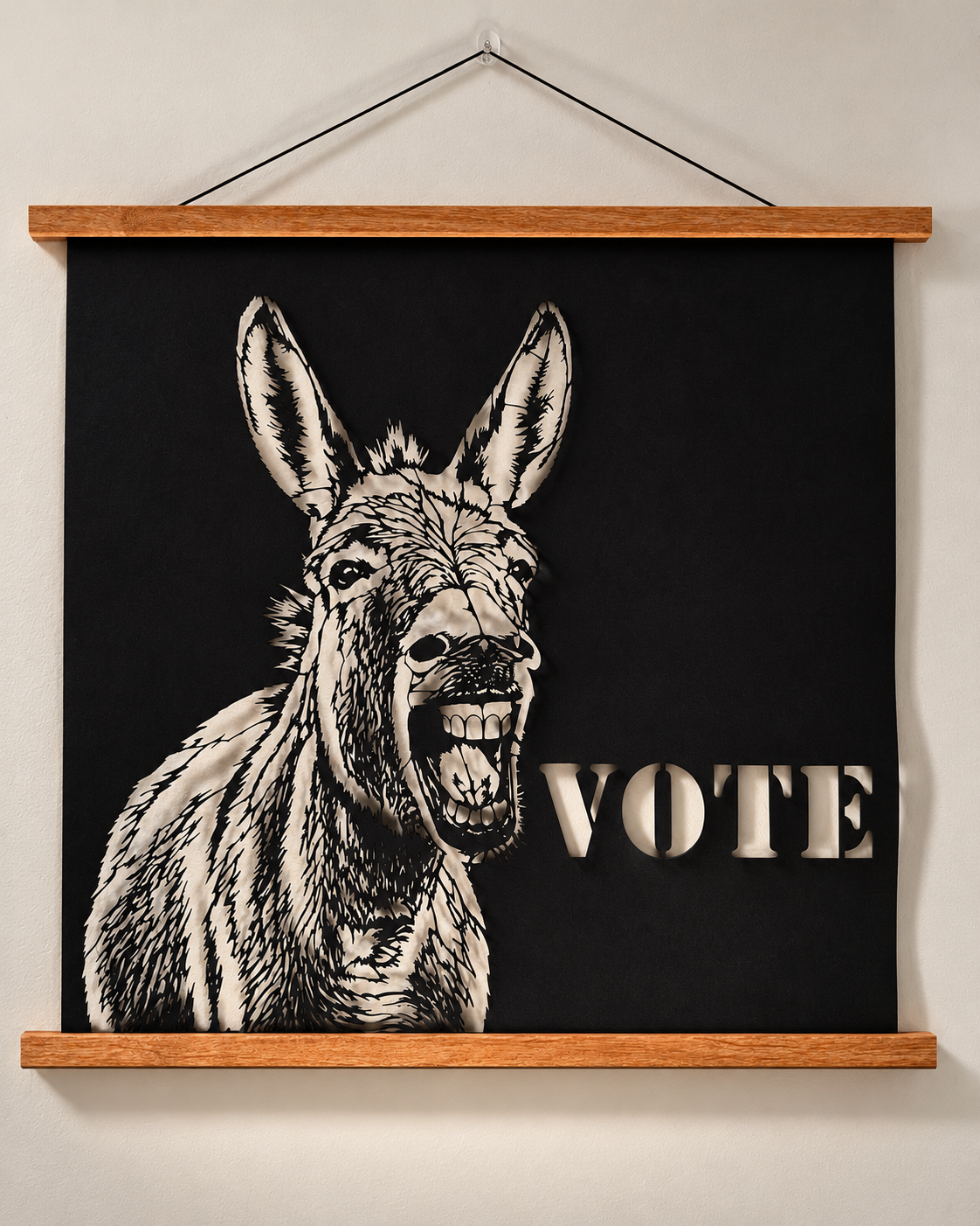 Ruthie political donkey VOTE poster, original black cut paper artwork displayed with a teak wood hanger, showing intricate cutouts and dimensional shadows against a softly lit studio wall.
