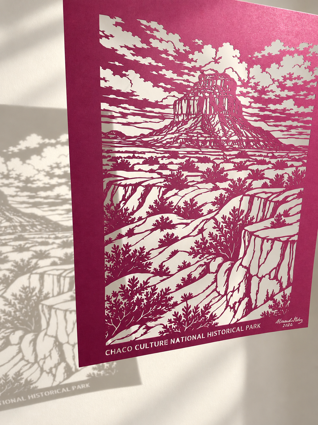 Chaco Canyon cut paper artwork by Alessandra Gutierrez casting intricate landscape shadows onto a sunlit wall.