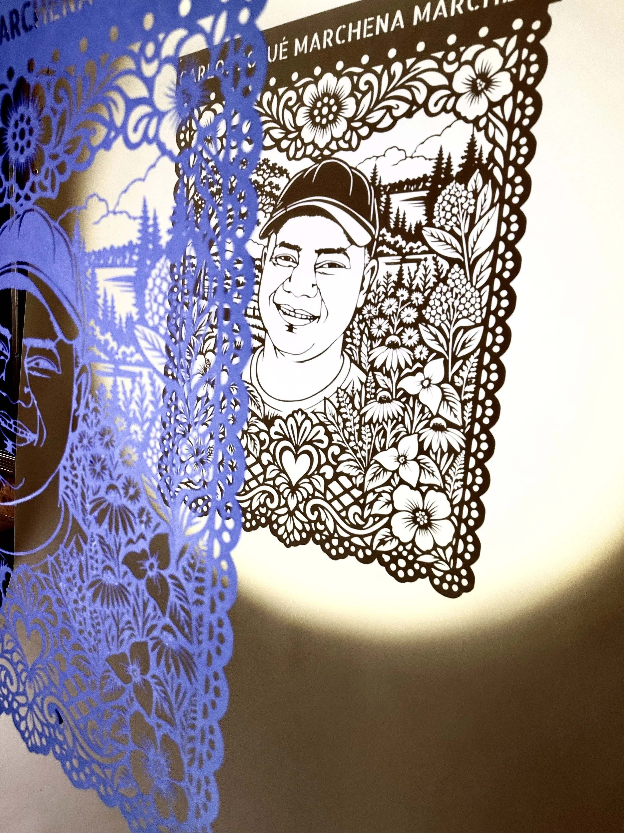 Papel Picado portrait at an angled view of Carlos Josué Marchena Marchena’s cut paper portrait casting a shadow on the wall.