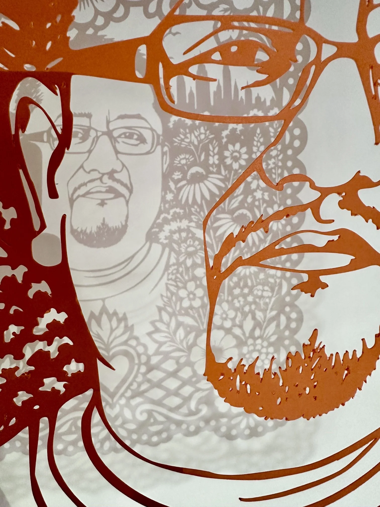 Extreme close up of Edwin Jeovanny López Cornejo’s orange papel picado portrait, showing his glasses, facial details, and the shadow cast by the cut paper design.
