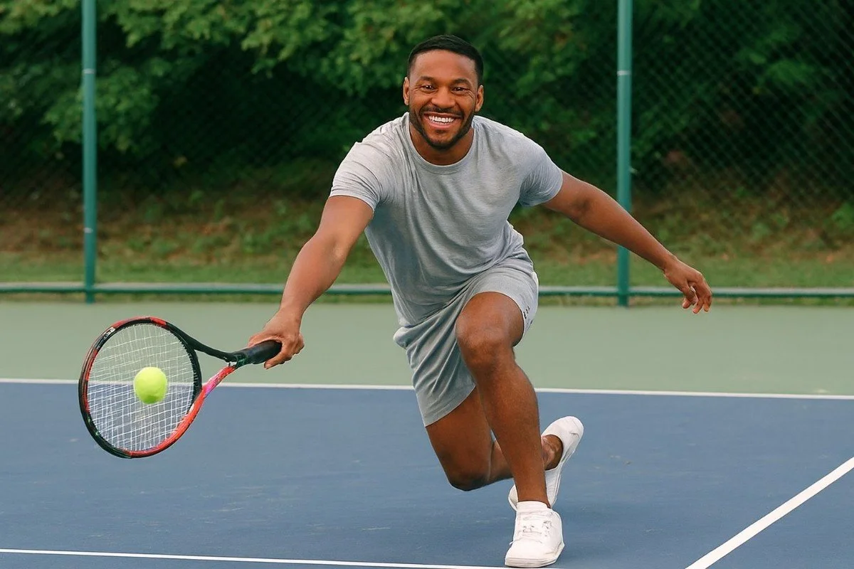 A middle-aged man lunges with confident energy on a tennis court, illustrating strength and recovery after leg surgery.