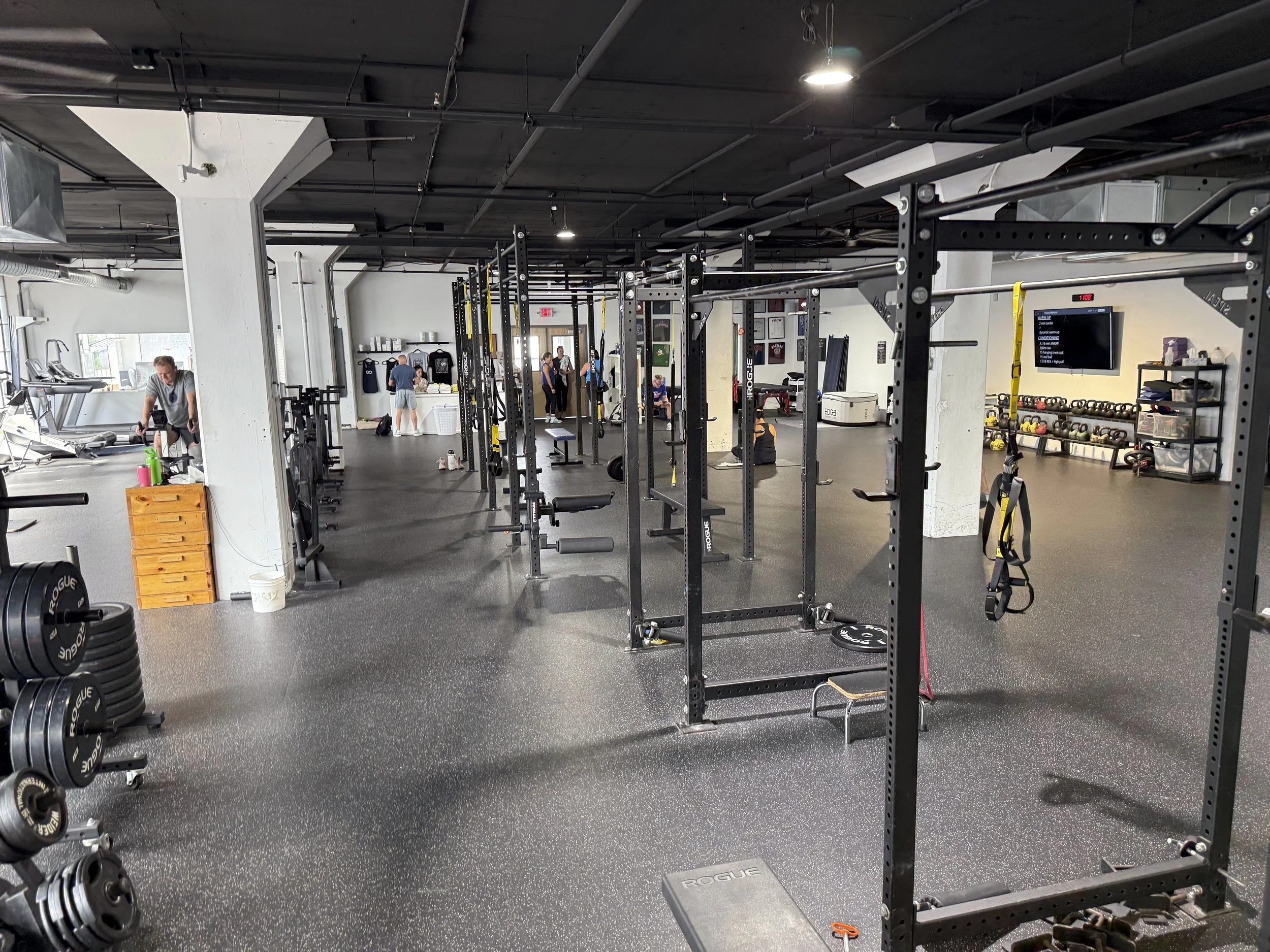 Fitness gym with weightlifting equipment, resistance machines, and people working out.
