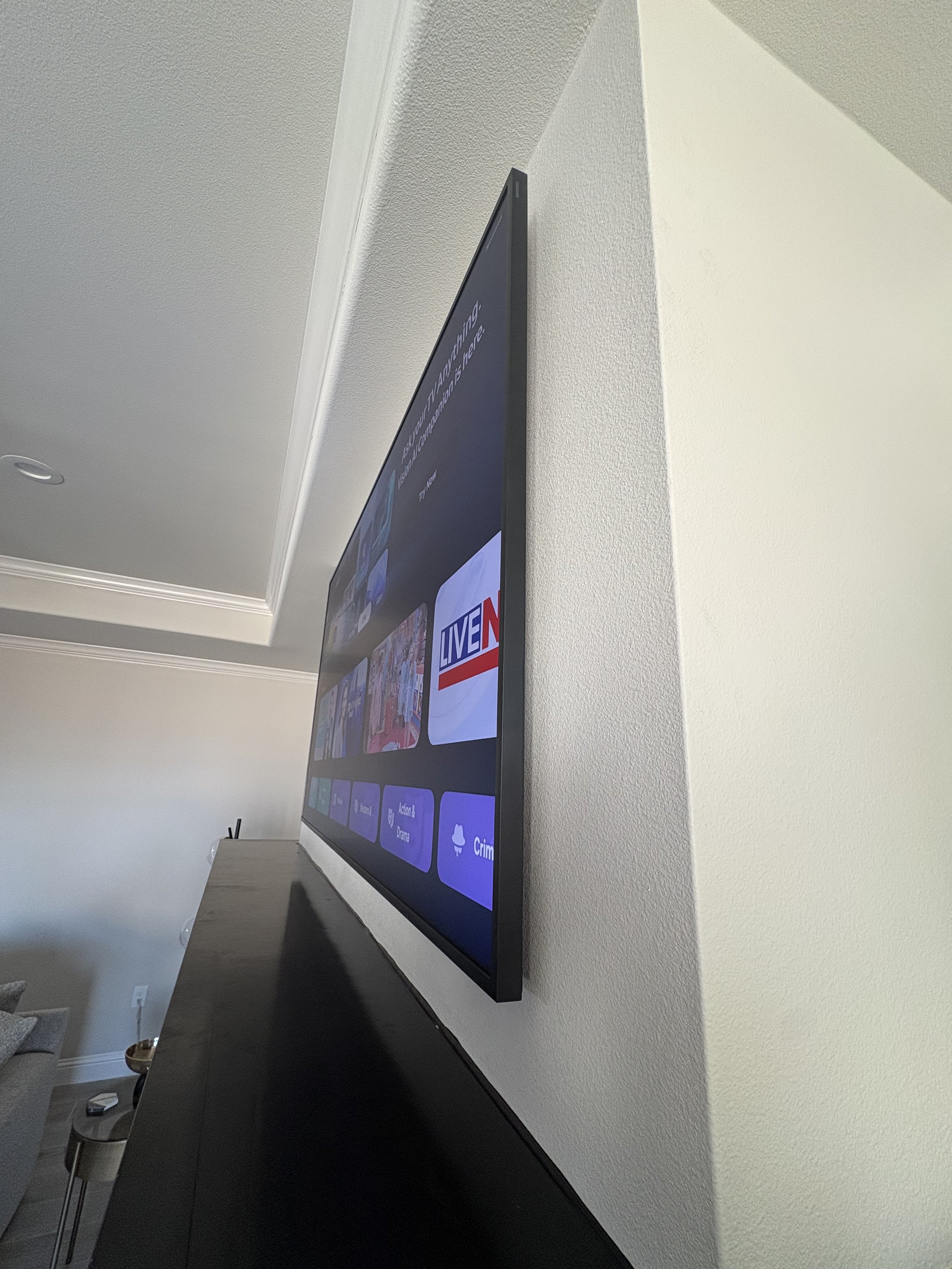 Flat-screen TV mounted on a white wall displaying a streaming service menu with various icons, including a live news logo.