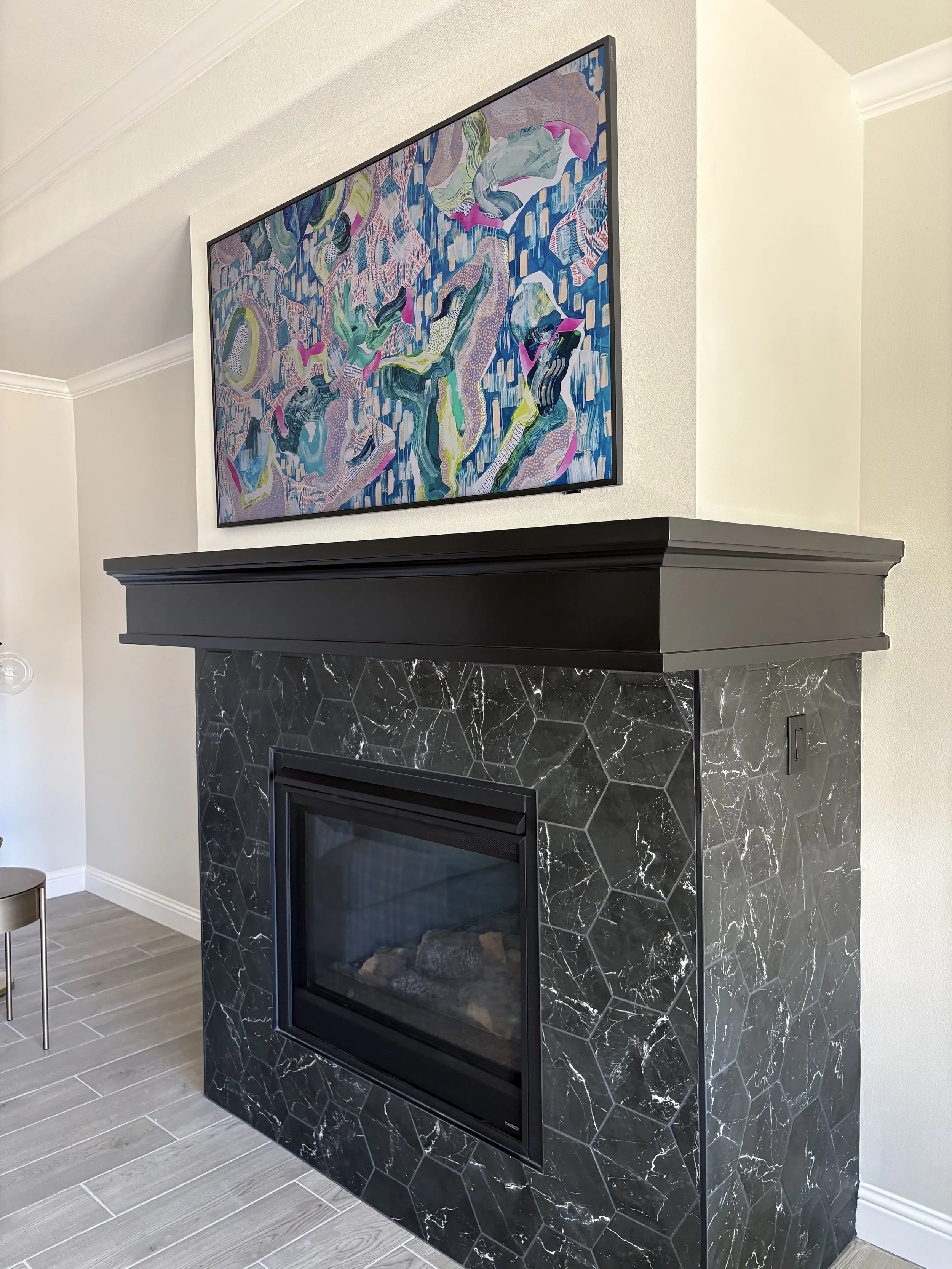 Colorful abstract painting hanging above a black marble fireplace with a black mantle in a living room.