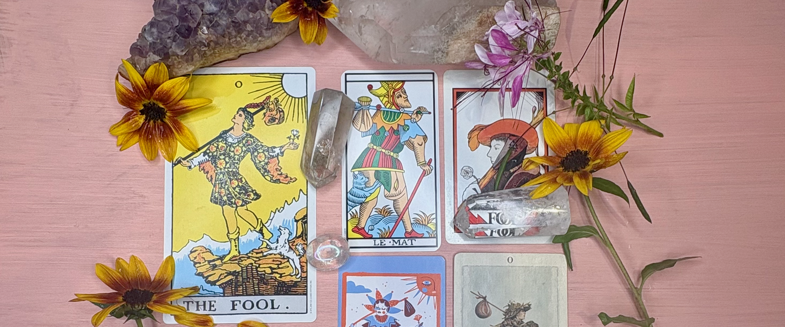 Tarot cards, crystals, and flowers arranged on a pink surface