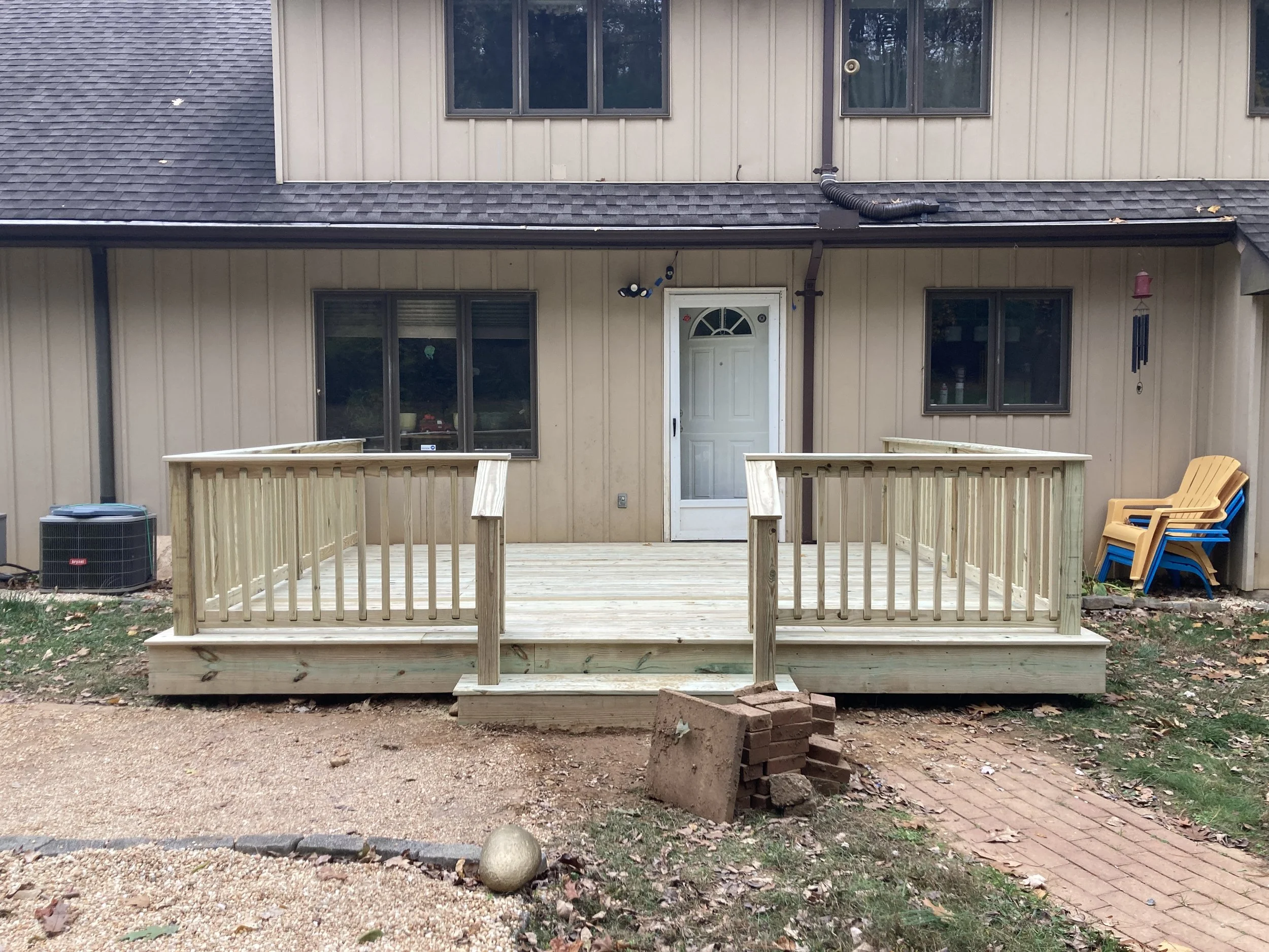 Newly built wooden deck attached to the back of a house, with four chairs stacked on the side and a brick on the ground
