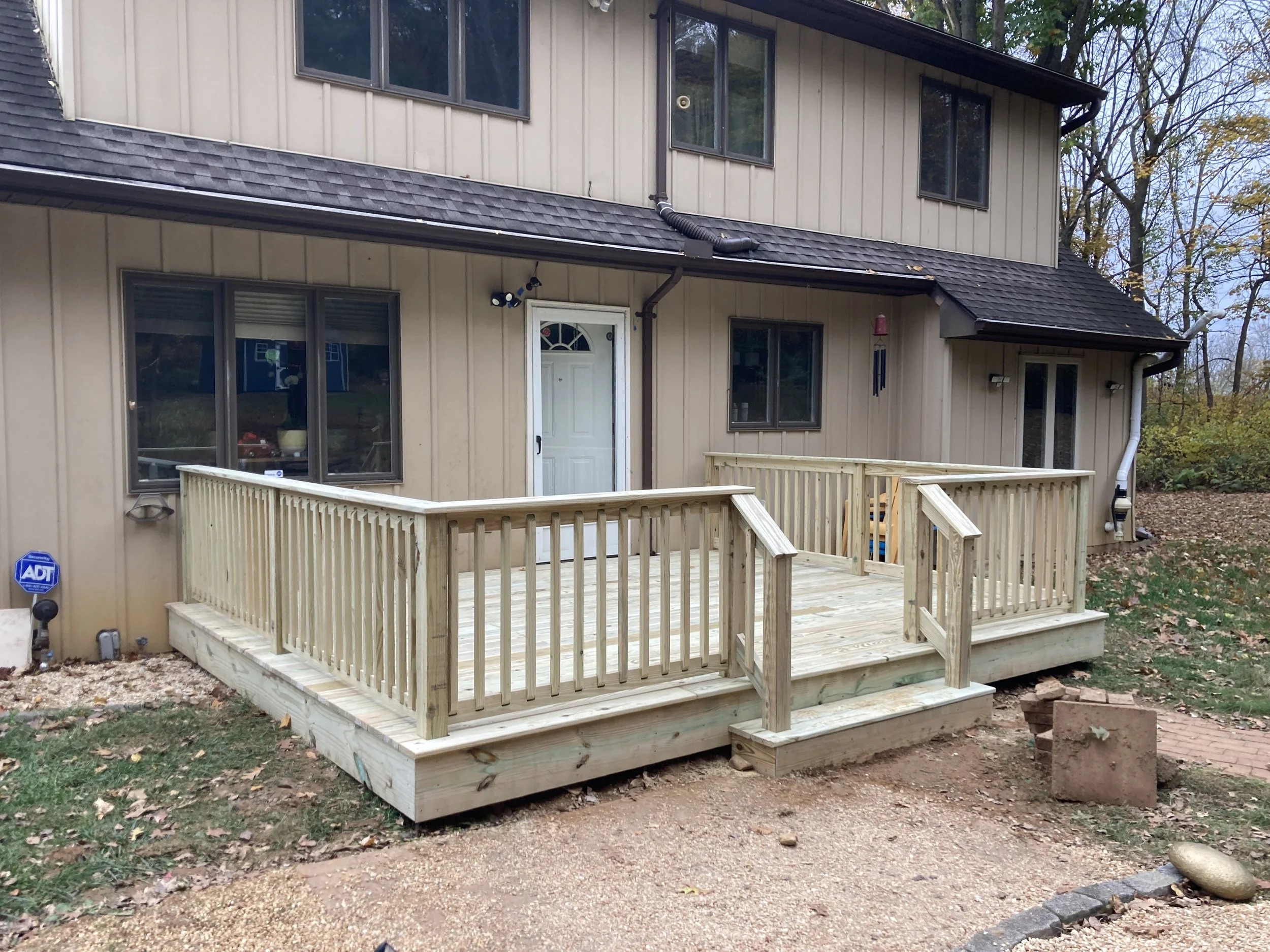 Newly built wooden deck attached to the back of a beige house with large windows.