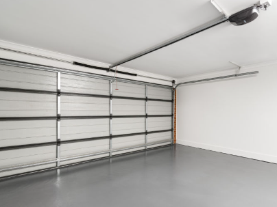 Empty residential garage with gray concrete floor and white walls, featuring a raised sectional garage door and automatic garage door opener.
