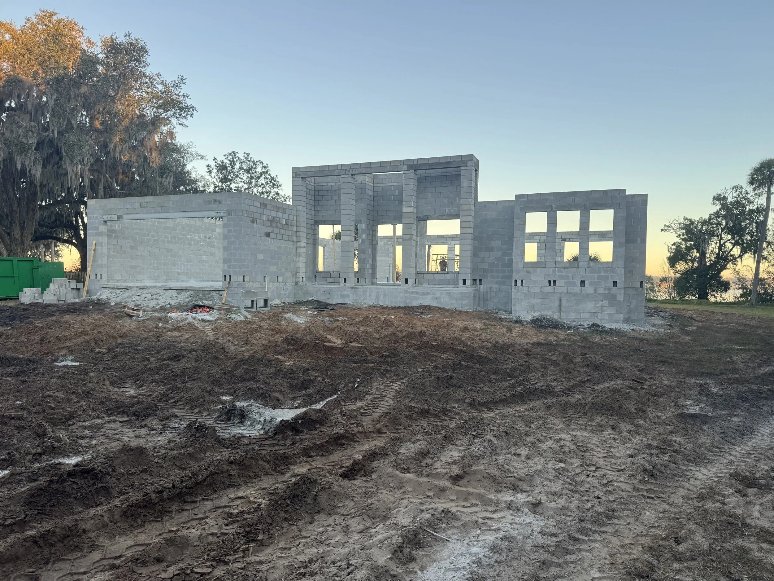 Construction site with a partially built concrete block structure on a dirt lot at sunset.