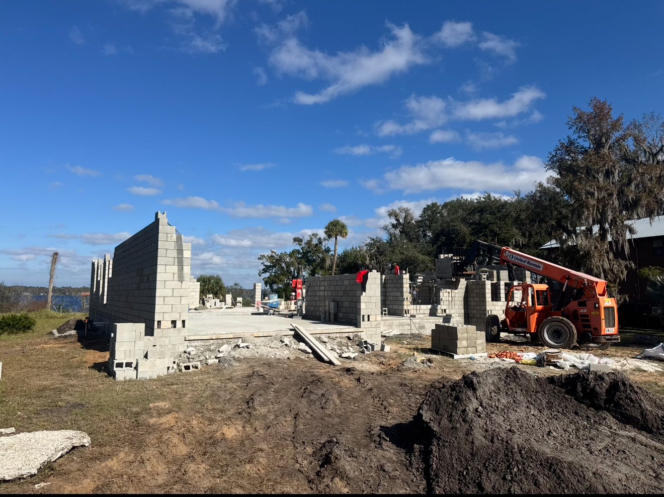 Construction site with partially built brick walls, a construction vehicle, and clear blue sky.