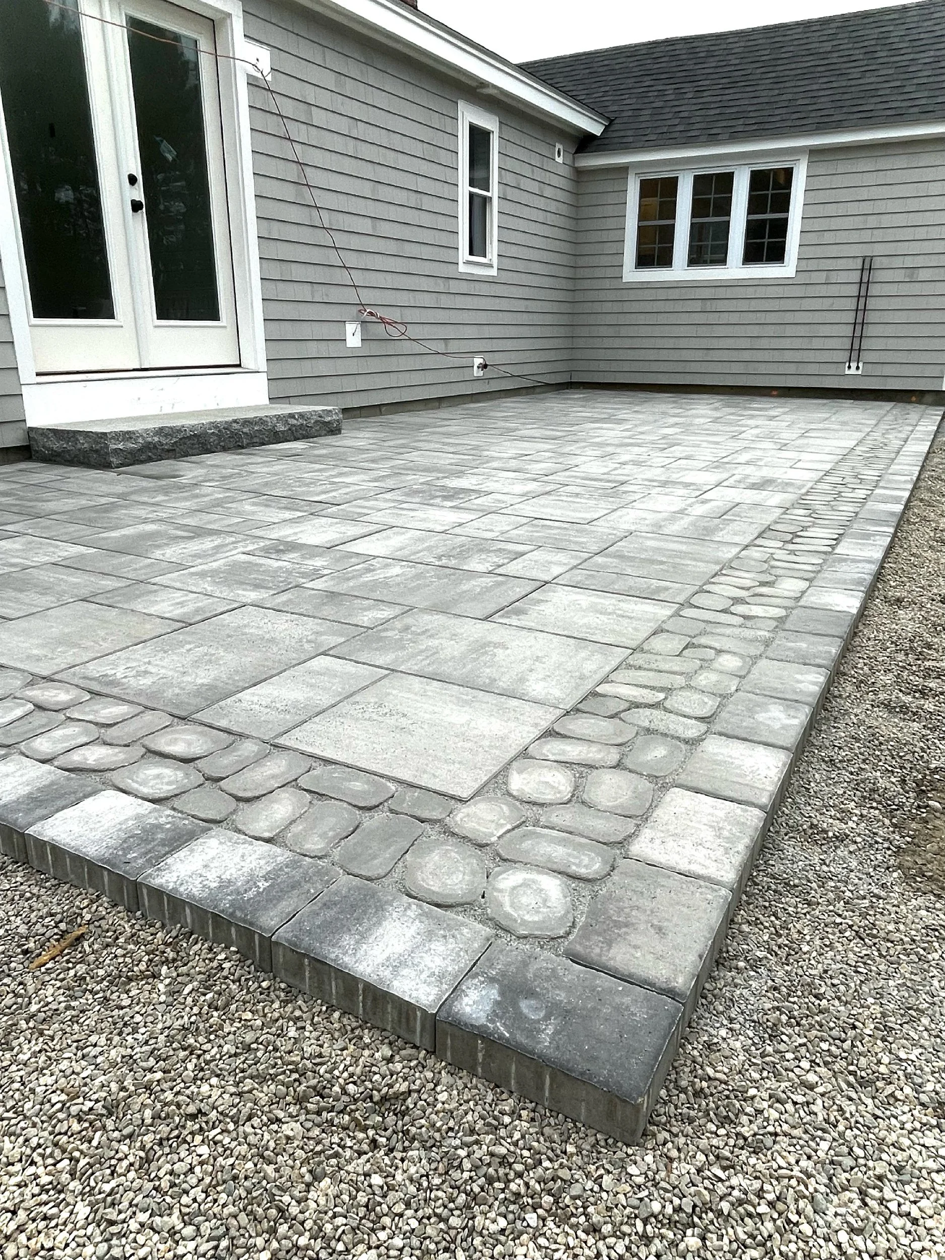 Gray limestone and river rock backyard patio built in Scarborough, Maine by The Englishmen Masonry