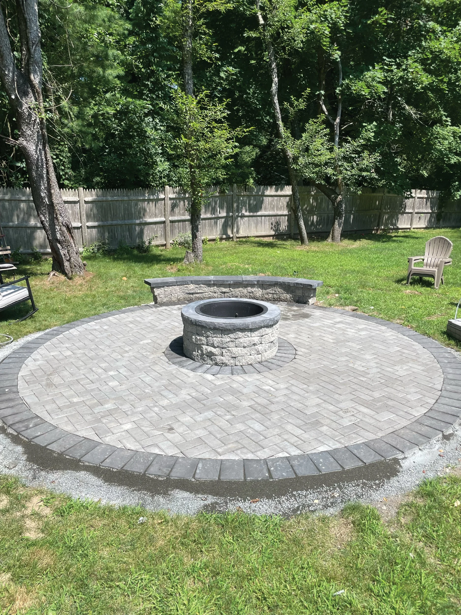 Circular patio and fire pit built with gray pavers and a dark border, hardscaping done by The Englishmen Masonry