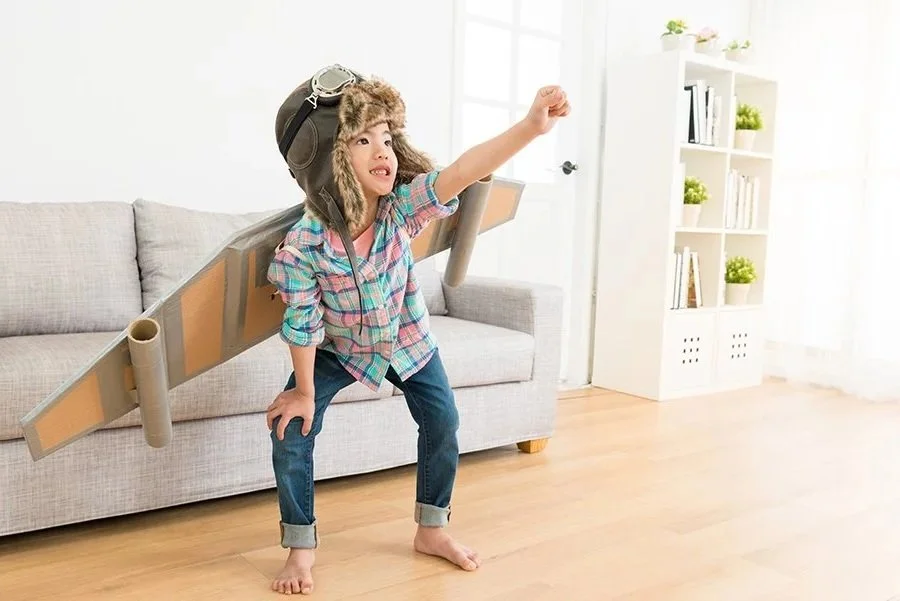 Child dressed as an airplane pilot with a cardboard airplane on their back, wearing a pilot's hat and goggles, playing during speech therapy for kids in Maui, HI.