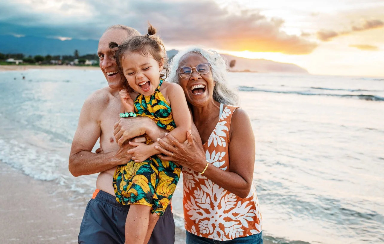 A joyful multigenerational family enjoying time together on the beach at sunset, with the grandmother able to participate in this activity thanks to cognitive therapy and occupational therapy for adults after stroke in Maui, HI.