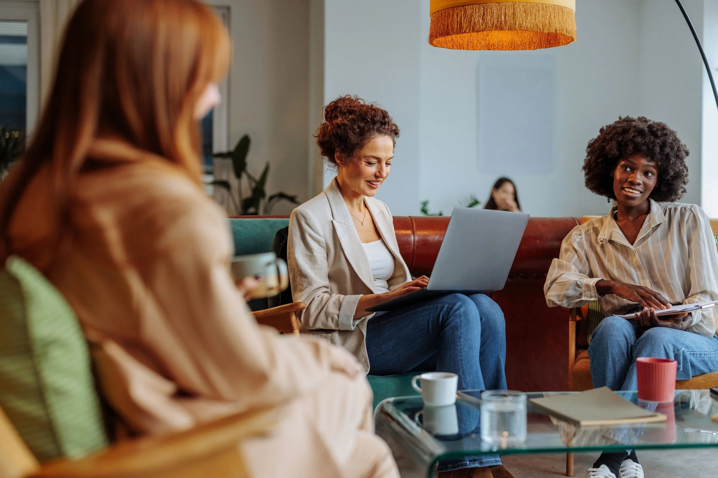 LGN Collab: Women having a discussion in a cozy, well-lit coffee shop with mugs and a laptop on the table.
