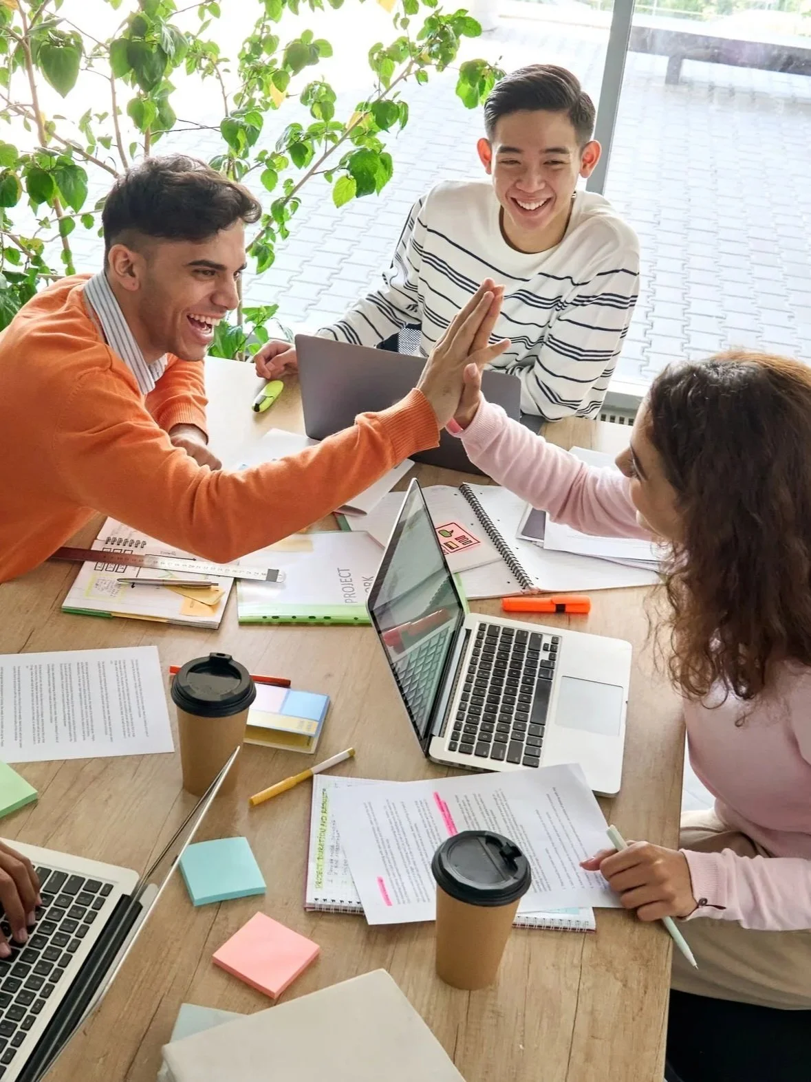 Team of three people working together in an office setting. Two of them high-fiving because of success in operational clarity.