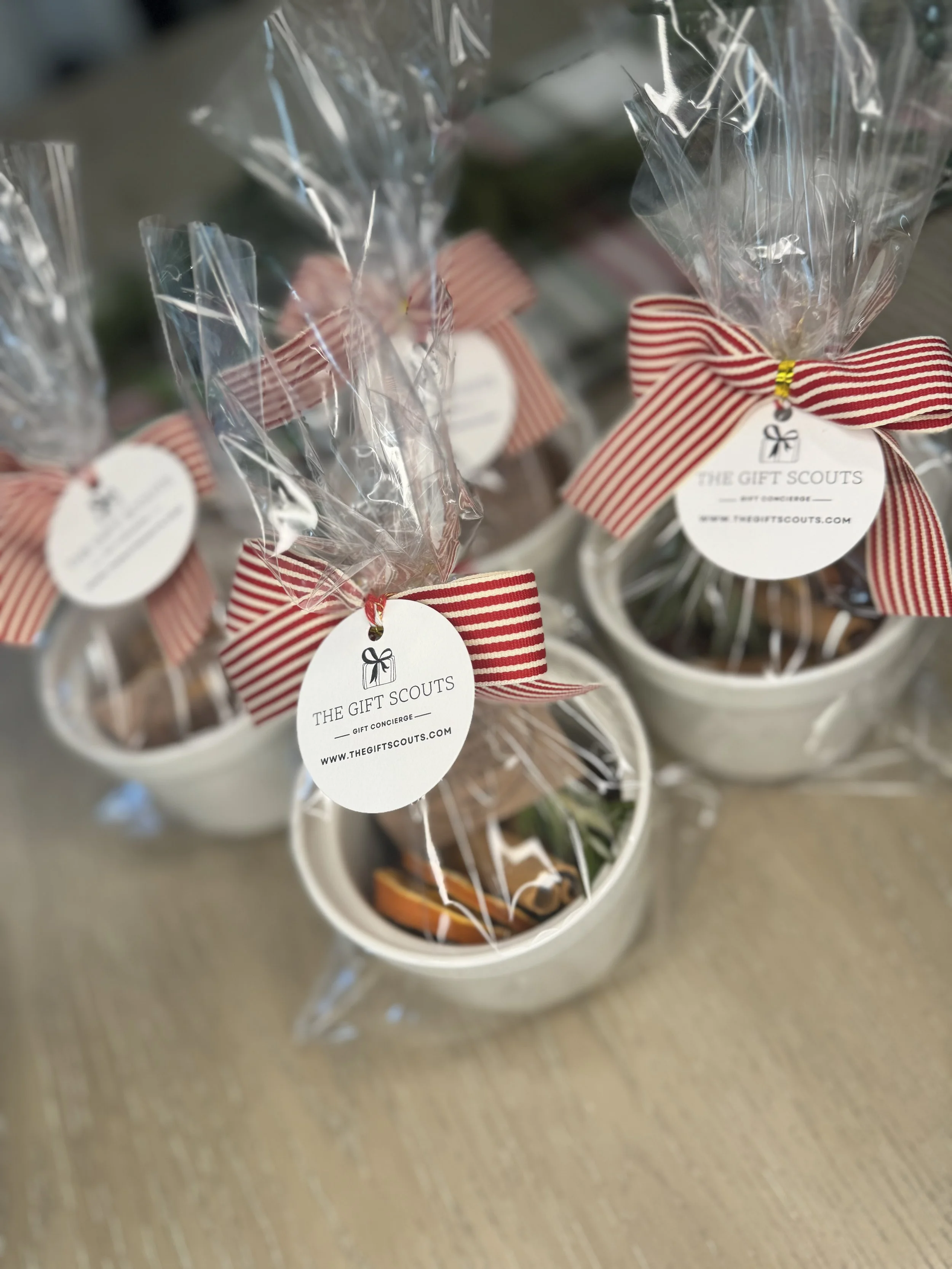 Small gift baskets with wrapped cookies or treats, decorated with red and white striped ribbons and tags reading 'The Gift Scouts' on a wooden surface.
