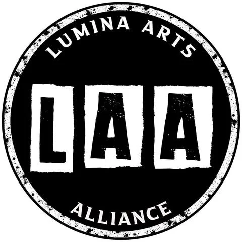 A circular black and white logo with 'LUMINA ARTS' at the top, 'ALLIANCE' at the bottom, and three large letters 'LAA' in the center.